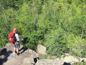 Hiker standing on a rocky outcrop looking down on a forest.