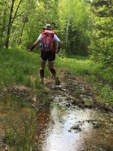 Hiker on a flooded, muddy hiking trail in the woods near Hartley Nature Center.
