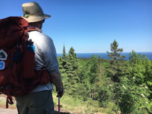 Man on hiking trail on mountaintop overlooking Lake Superior.
