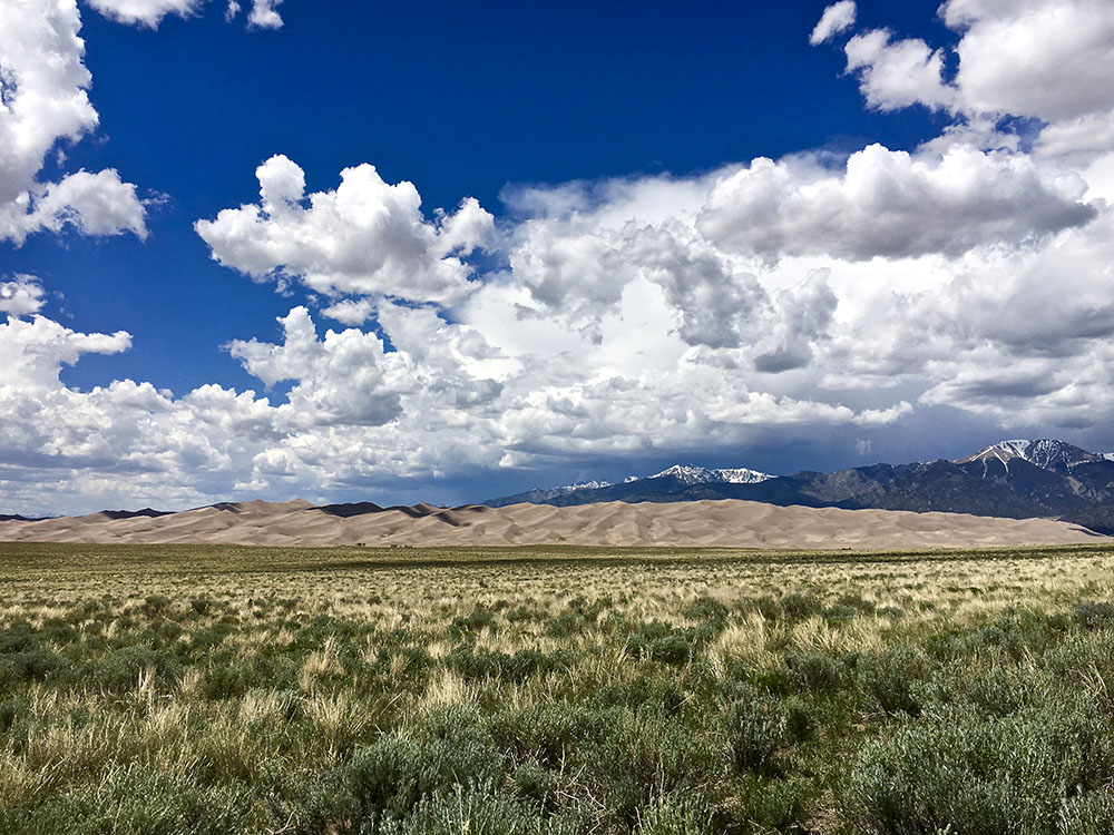 View of Great Sand Dunes National Park, with sand dunes in front of mountains.