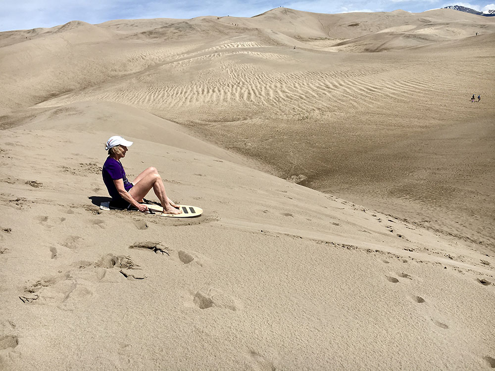 Woman sledding down sand dune at Great Sand Dunes.