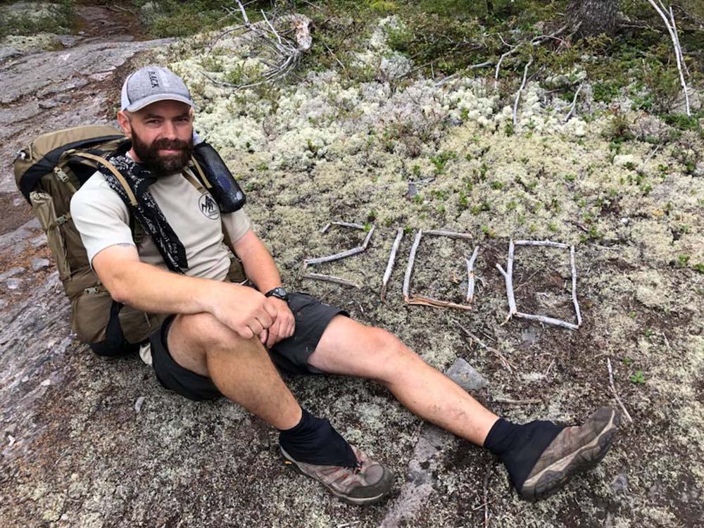 Hiker sitting on ground by number 200 made of sticks, part of Warrior Expeditions program.