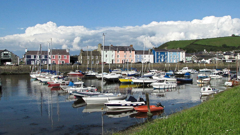 Village along Wales Coast Path with colorful homes and boats in harbor.