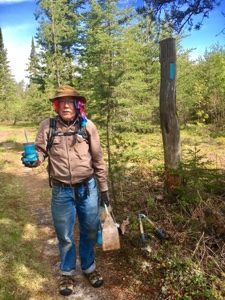 Man standing on North Country Trail near Pine River holding blue paint near a blue blaze.