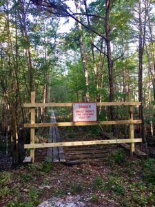 Hiking trail bridge blocked off with a gate with a sign that says it's unsafe.