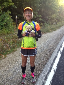 Woman in neon yellow vest standing on the side of the road holding a teddy bear on the Ice Age Trail near La Budde Creek.