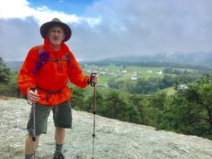 Male hiker in orange coat standing on top of rocky outcrop with spacious view near Reed Gap on the New England Trail