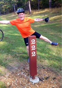 Male cyclist standing on one leg in front of Natchez Trace mile marker 222.