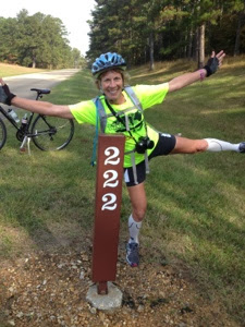 Female cyclist standing on one leg in front of Natchez Trace Mile Marker 222.