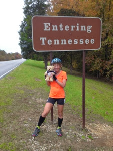 Female cyclist standing by sign saying Entering Tennessee, along the Natchez Trace.