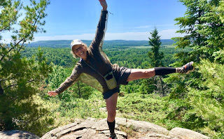 Woman hiker standing on one leg with arms outstretched on top of rocky outcrop on Superior Hiking Trail