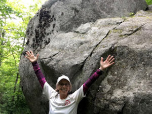 Woman standing in front of giant glacial erratic with her hands up in the air.
