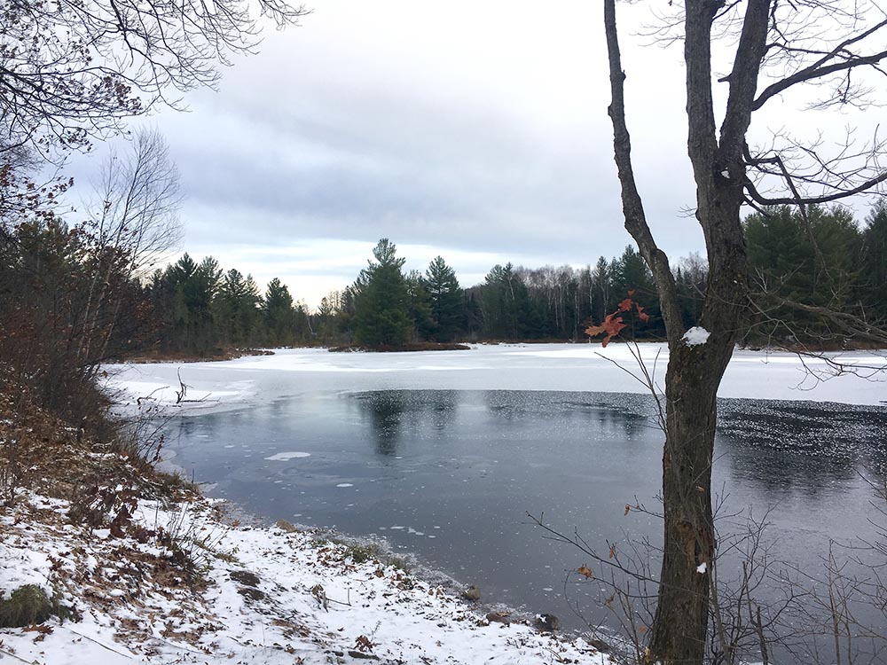 A partially frozen lake, surrounded by snow, in the Harrison Hills segment of the Ice Age Trail.