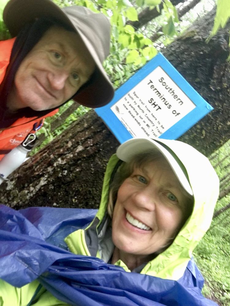 Water-logged male and female hikers standing by sign marking the southern terminus of the Superior Hiking Trail.