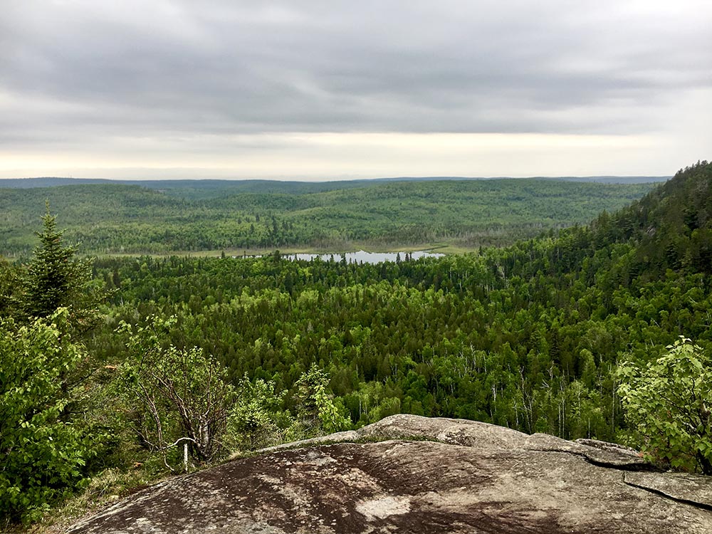 Expansive view over forestland with water in the distance from a rocky outcrop along the Superior Hiking Trail.