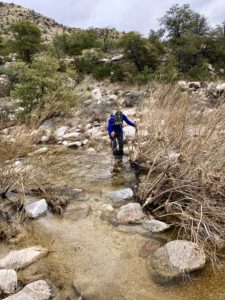 Hiker crossing rock-filled creek on the Arizona Trail near Summerhaven.