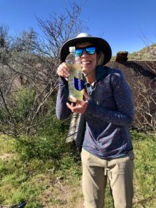 Female hiker on Arizona Trail at Beehive Well and holding a bottle of yellow water.
