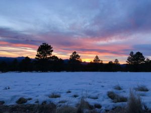 A field on top of a mountain north of Flagstaff that's covered with snow with a pink, yellow and orange sunset in the background.