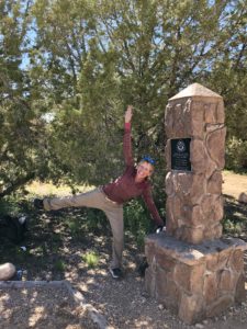 Woman making a star pose on one leg at the Arizona Trail's northern terminus marker.