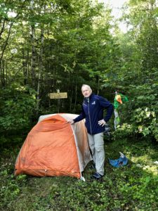 Man standing by orange tent at Lake Ruth trailhead, North Country Trail.