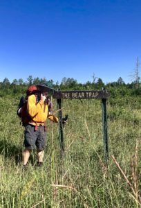 Male backpacker standing next to wooden sign reading, "The Bear Trap" near Gordon Dam, Wis.