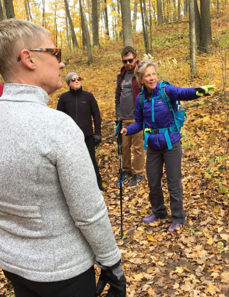 Female hiking guide pointing out a feature in the woods during the fall.