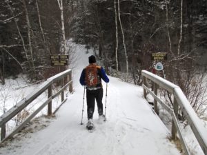Snowshoer crossing wooden bridge on Timm's Hill Trail