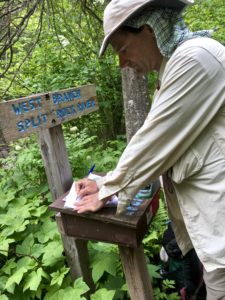 Man with a wide-brimmed hat signing a trail register.