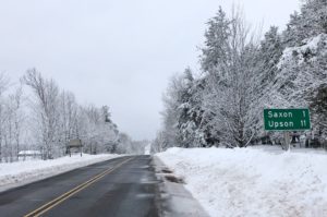 Paved road through snowy countryside with road sign for Saxon, Wis.