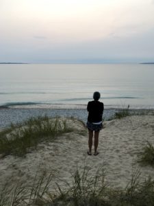 Person standing on the beach in front of Lake Michigan as the sun sets.