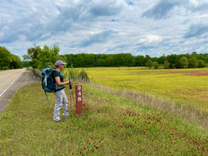 Female hiker standing by mile marker in sea of wildflowers on Natchez Trace near Blackland Prairie.