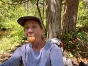 Woman sitting near a creek with a clementine in her mouth.