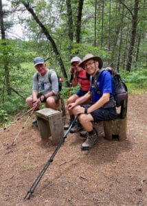 Three hikers sitting on tree stump chairs near Townline Road and Spring Lake on the NCT.
