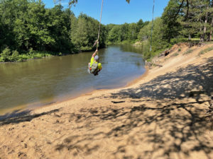 Hiker swinging on rope over Manistee River.