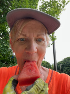 Woman in orange shirt eating a slice of watermelon.