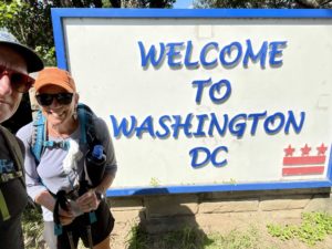 Two people standing by “Welcome to Washington DC” sign.