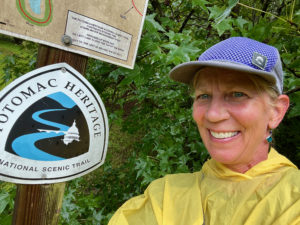 Woman in rain poncho by Potomac Heritage Trail sign.