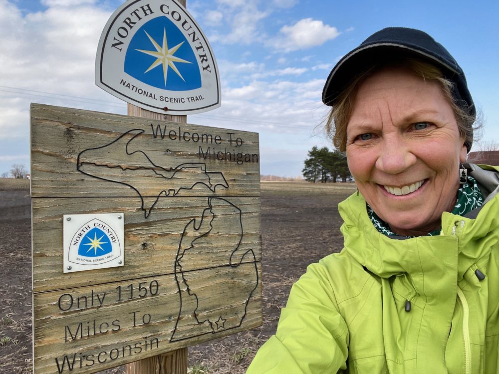 Woman standing by North Country Trail sign for Michigan.