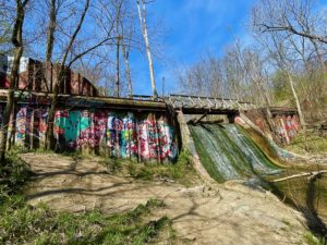 Dam with waterfall and colorful graffiti on metal framing.