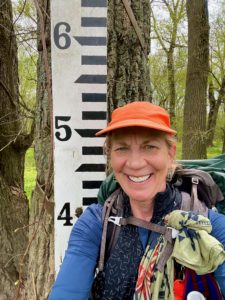Woman in the woods by a flood gauge.