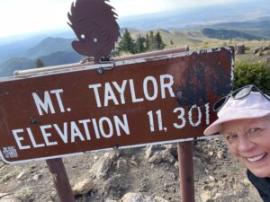 Hiker standing by sign saying Mt. Taylor Elevation 11,301’